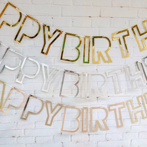 Close-up of Happy Birthday banners in gold, silver, and rose gold on a white brick wall