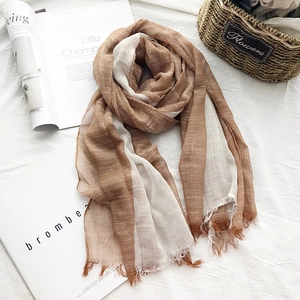 Flat lay of a thin brown and white cotton linen scarf with tassel edges and a magazine