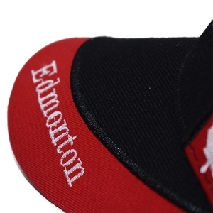 Macro view of white Edmonton embroidery on a red and black twill cotton baseball cap