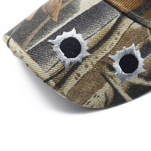 Detailed macro view of camo baseball cap brim with bullet hole embroidery accents