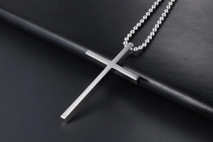 Close-up of a silver titanium steel cross pendant necklace on a black leather background