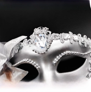Macro detail of silver masquerade mask with ornate gemstone and feathered lace trim