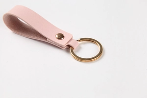 Close-up of pink lychee grain leather keychain with polished gold metal ring and rivet