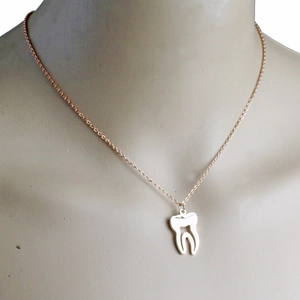 Gros plan d'un collier pendentif dent ajouré en or rose porté sur un mannequin