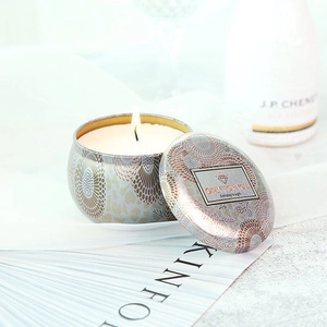 Close-up of a burning scented soy candle in a decorative tin with elegant champagne hues