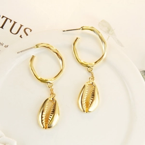 Detail of gold irregular hoop earrings featuring a polished seashell charm on ceramic tray