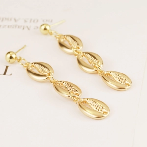 Macro detail of golden seashell drop earrings featuring triple-linked alloy nautilus shells