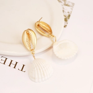 Detailed view of golden cowrie shell and white scallop earrings on lifestyle background