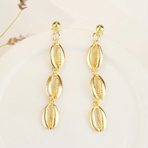 Detail of gold-plated triple shell drop earrings on a white ceramic plate with lavender