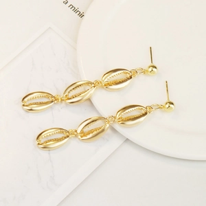 Detail of golden bohemian shell drop earrings with three tiered conch charms on marble background