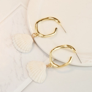 Detail of bohemian gold-finish shell drop earrings on a marble and ceramic background