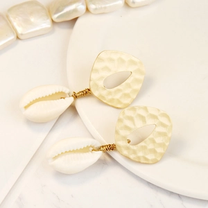 Detail of bohemian gold alloy earrings with hammered texture and natural cowrie shells