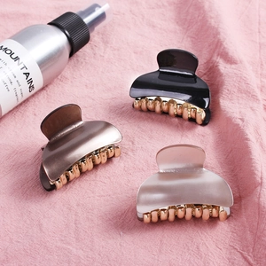 Set of three acrylic hair claws in black, amber, and grey on a textured pink fabric