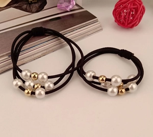 Detailed view of elastic hair ties with white pearls and gold beads on a table