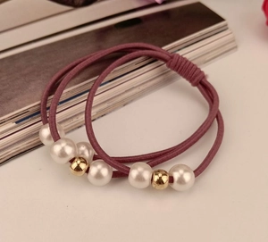 Close-up of two dusty pink elastic hair ties with pearls and gold beads on a white surface