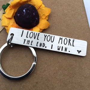 Macro shot of silver rectangular keychain engraved with I Love You More on kraft paper
