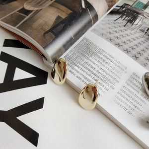 Detail of high-polished gold oval studs with a fluid pebble shape on a fashion magazine