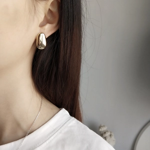 Close-up of model wearing polished golden organic water-drop stud earrings in 925 silver