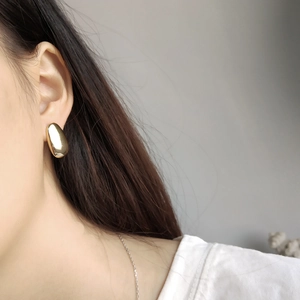Close-up of minimalist golden bean earrings worn on an ear to show size and fit