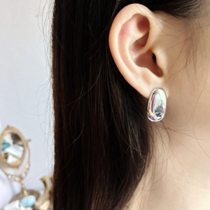 Close-up of minimalist oval silver earring worn by model in a soft home setting
