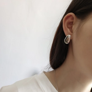 Close-up of minimalist oval silver studs with a polished mirror finish on a model's ear