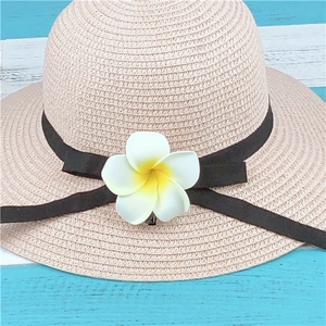 Pink straw sun hat with black ribbon and plumeria flower on blue striped background
