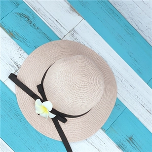 Women's summer straw sun hat with plumeria flower detail on blue wood background