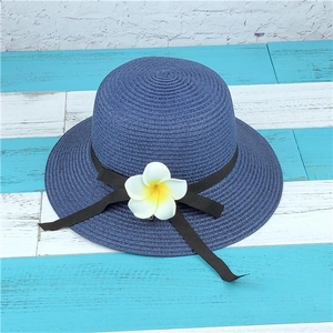 Close-up of navy straw sun hat featuring a white frangipani flower and black ribbon bow