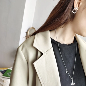 Detailed view of silver Saturn orb necklace and square earrings on a model in beige suit