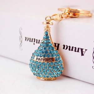 Golden perfume bottle keychain with blue rhinestones on a white surface closeup