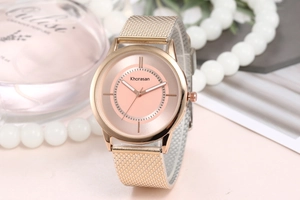 Detail of rose gold mesh watch with pink dial next to pearls and perfume bottle