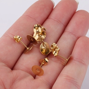 Close-up of gold-plated stainless steel flat pad earring posts held in palm for scale