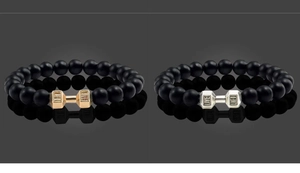 Close-up of matte black bead bracelets with gold and silver dumbbell-shaped pendants