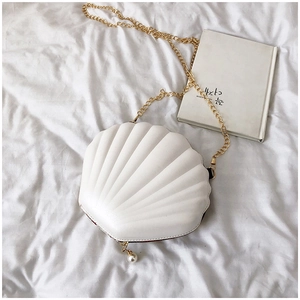 Detail of white shell-shaped handbag with embossed texture, gold chain and pearl charm