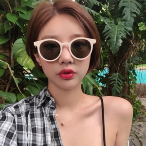 Model wearing round milk tea beige sunglasses with dark lenses in a tropical setting