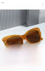 Detail of amber tortoiseshell cat-eye sunglasses with silver rivets on a white podium