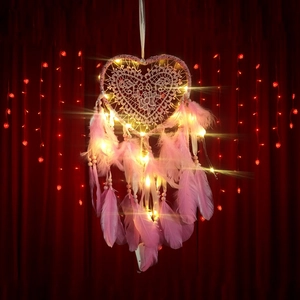 Pink heart-shaped dreamcatcher with LED lights and feathers on a red backdrop