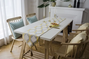 Detail of yellow and grey geometric jacquard table runner with decorative tassels on ends