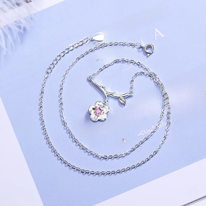 Silver cherry blossom branch necklace with pink gemstones on light blue background