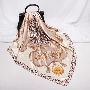 Elegant silk-like scarf with leopard chain print draped over a black designer handbag