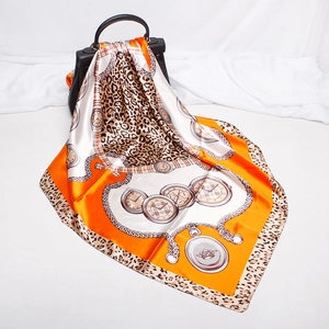 Detailed shot of an orange silk square scarf featuring leopard and chain prints on a black bag