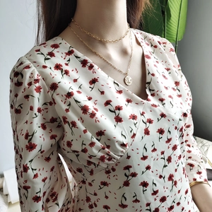 Detailed view of dual-layered gold necklaces with round relief pendant on floral V-neck dress