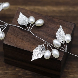 Macro detail of silver leaf and pearl bridal headband on rustic dark wood base