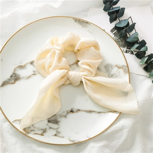 Detail of cream silk scrunchie with long ribbons on marble tray with eucalyptus leaves