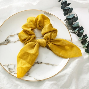 Detailed view of yellow satin bow hair tie on a white marble tray with eucalyptus