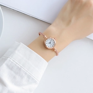 Close-up of rose gold wire mesh strap and white dial with Arabic numerals for women