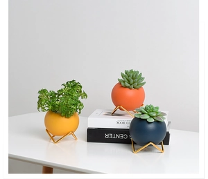 Three ceramic succulent pots in yellow, orange, and blue with gold geometric metal stands