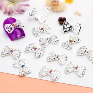 Hollow silver bow nail art charms with AB rhinestones on a purple nail design