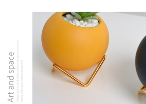 Close-up of a yellow matte ceramic planter on a gold metal tripod stand with succulents