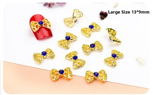 Macro detail of large gold hollow bow nail charms with blue rhinestones on red nails